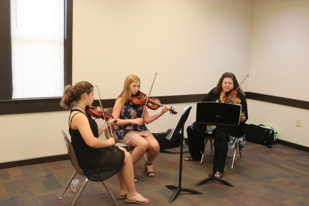 Three women seated playing violins