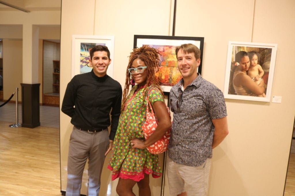 Artists Isaac Alcantar, Tokie Rome-Taylor, and Miles Davis in front of a painting by Alcantar