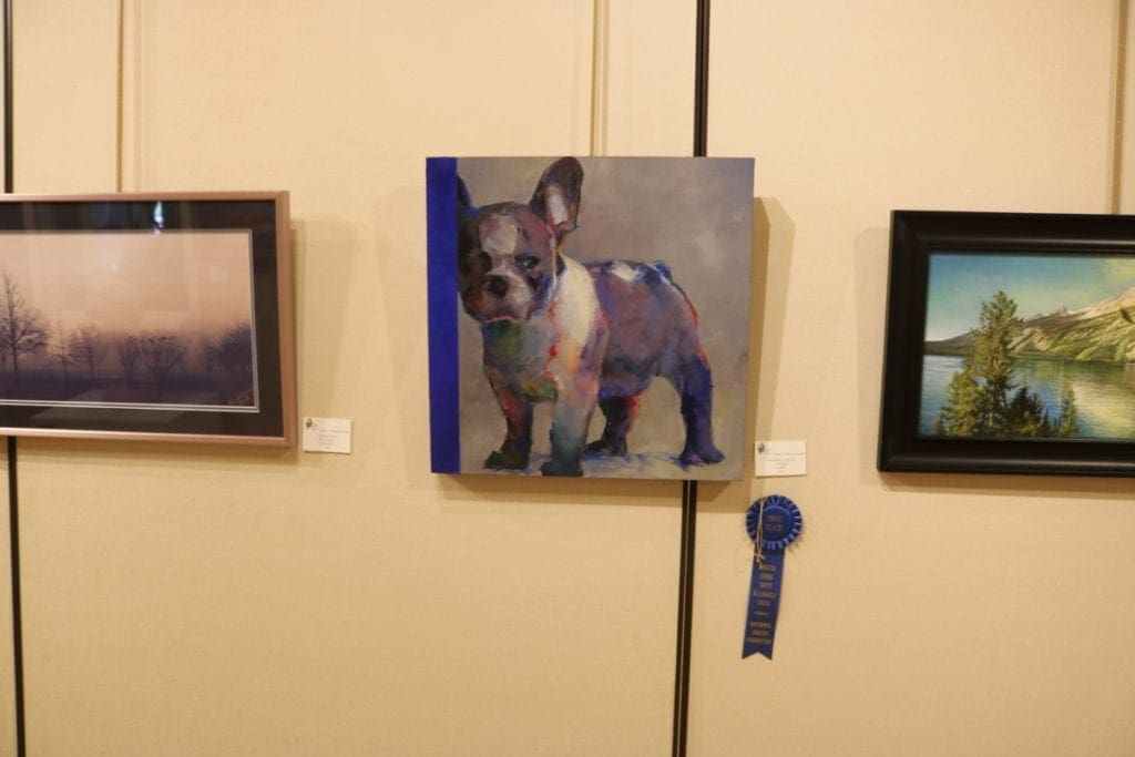 Grand Prize entry "French Blue," by NancyJeanette Long. The painting is of a stocky dog with large upright ears staring ahead with a skeptical expression. The painting has a significant amount of the color blue.