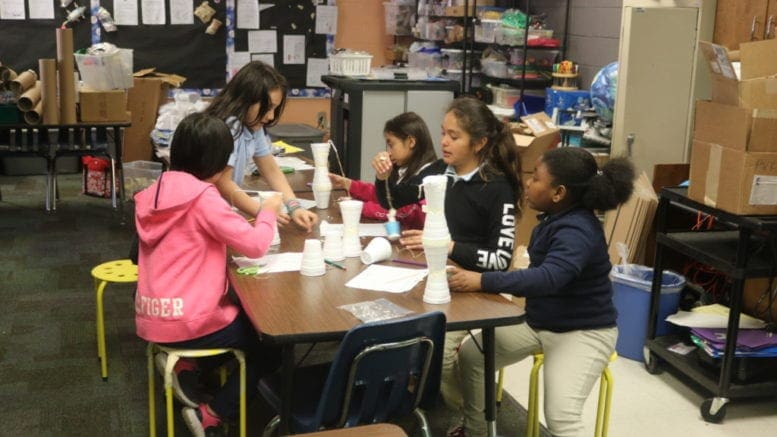 Children around a table building cranes from styrofoam and other common materials for a STEM project.