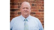 Doc Eaton in shirt and tie, standing in front of a red brick buiding