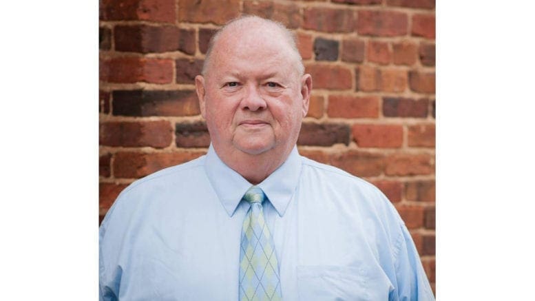 Doc Eaton in shirt and tie, standing in front of a red brick buiding