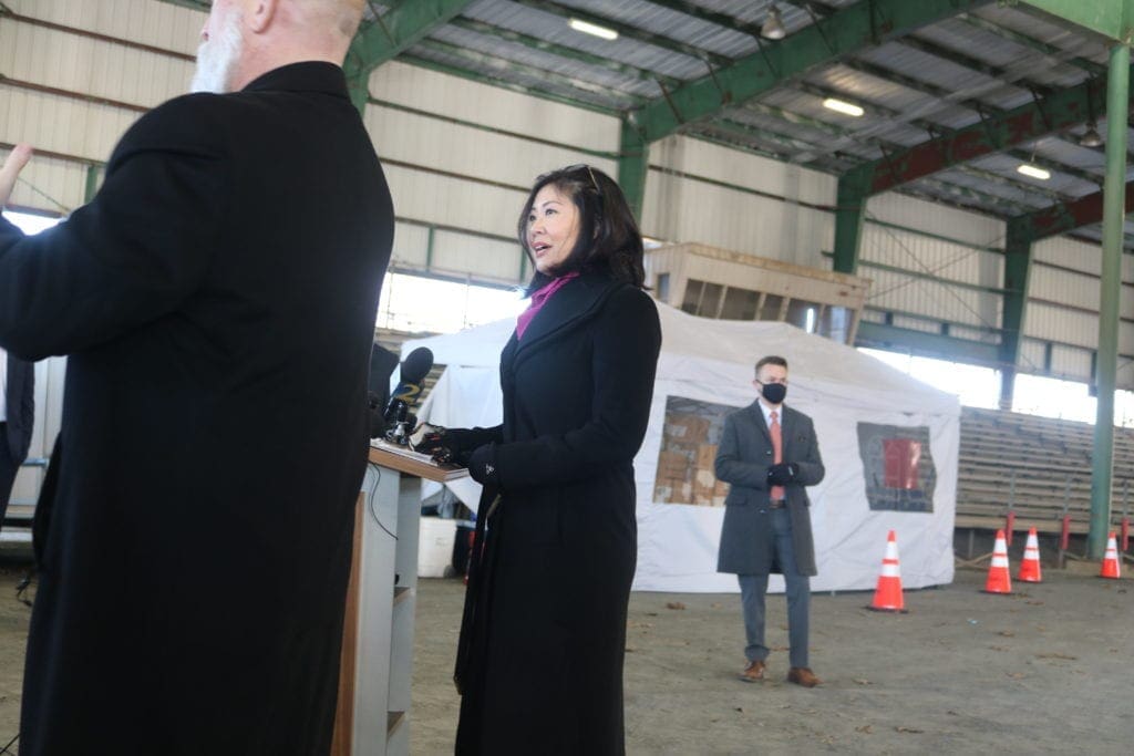 Dr. Janet Memark wearing long coat stands in front of microphones at press conference