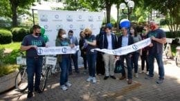 Ribbon cutting for bike share station. A group of people hold a long ribbon