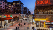 Looking down a street at night in The Battery. Stores and apartments flank the street, which is filled with pedestrians.