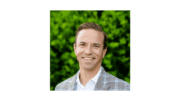 Headshot of Tim Chamberlain, white shirt no tie , plaid jacket, leafy green backdrop