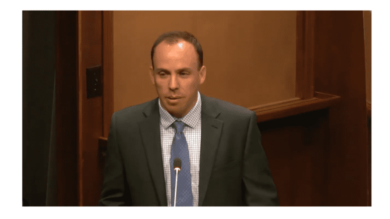 Drew Resslaer in suit and tie standing at podium