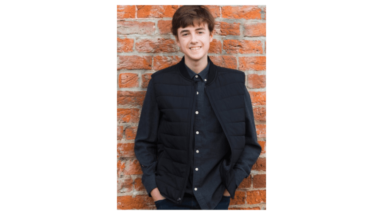 Student musician and composer Will Weaver standing against brick wall