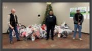 Three Plant McDonough employees stand in front of a Christmas tree with presents, smiling