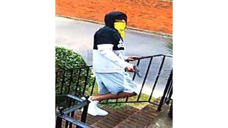 man with mask walking up exterior stairs with gun