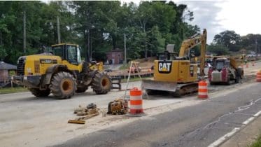 Road construction equipment on shoulder of road with orange safety barriers