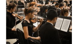 Youth orchestra rehearsing with young woman violinist in black dress in focus