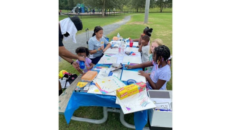 A group of children doing craft activities with markers and maps around an outdoor table