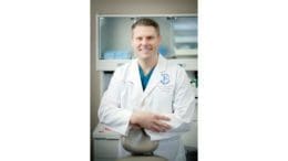 Dr. Terry Hooper in dental office wearing white medical jacket, smiling.