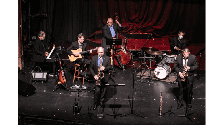 A six-person jazz ensemble performing: keyboards, 2 saxophones, guitar, drums, standing bass