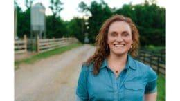 Holly McCormick smiling in short sleeve shirt on rural road bordered by wooden fences