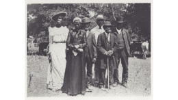 In an obviously old photo a line of Black men and women in formal dress posing for photo .