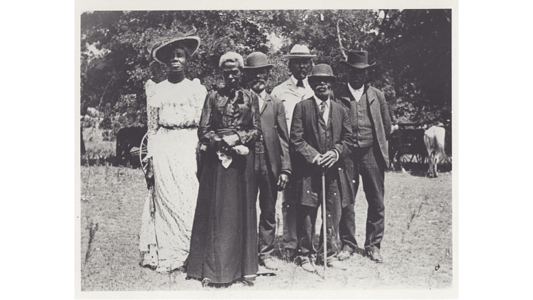 In an obviously old photo a line of Black men and women in formal dress posing for photo .