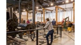 Young woman leans on fence around museum display of machinery