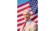 Charles Lutin in suit standing in front of large American flag