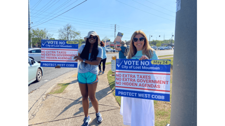 Two women holding up signs opposing Lost Mountain cityhood