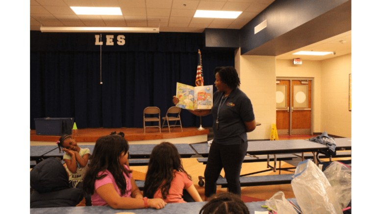 woman with an open book talking to group of children in a classroom