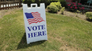 sign with American flag stating "Vote Here"