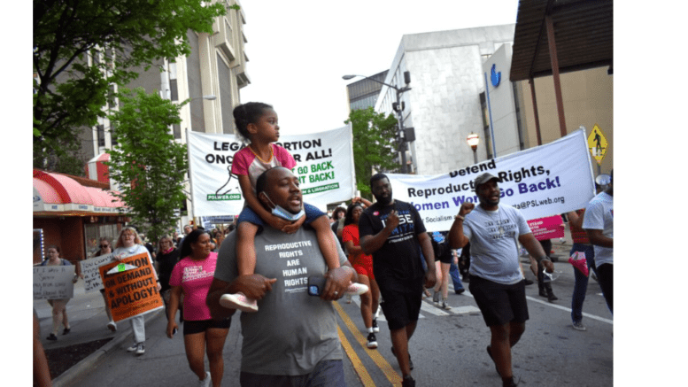 a group of people marching in protest, one man with a smaill child on his shoulders