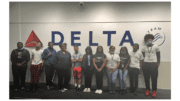 11 teens in front of a large DELTA Airlines sign
