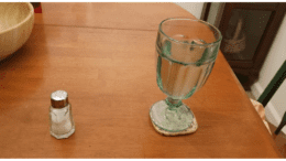 a shaker of salt and a glass of water on a wooden table