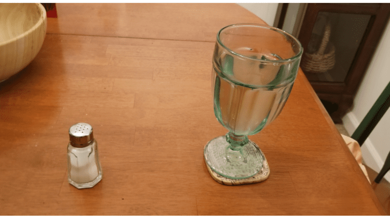 a shaker of salt and a glass of water on a wooden table