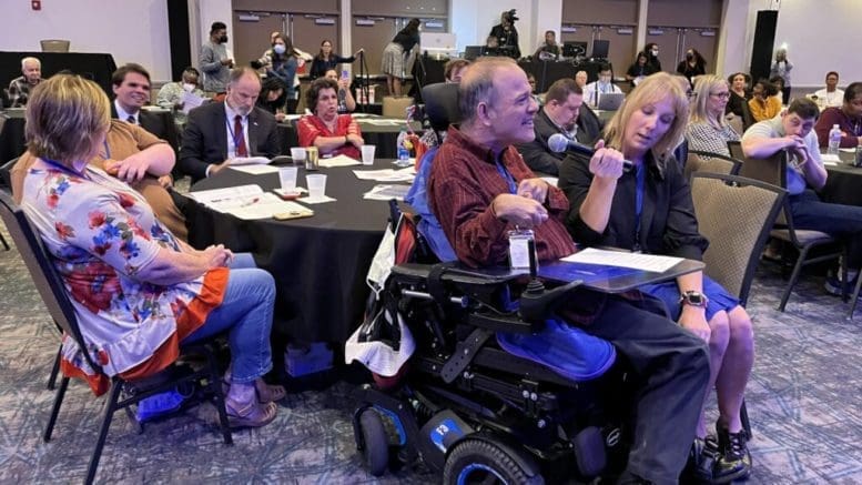 A person in a motorized wheelchair speaks into a microphone