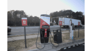 An electric vehicle charging station on Riverside Parkway, a moving tractor-trailer visible on the roadway.