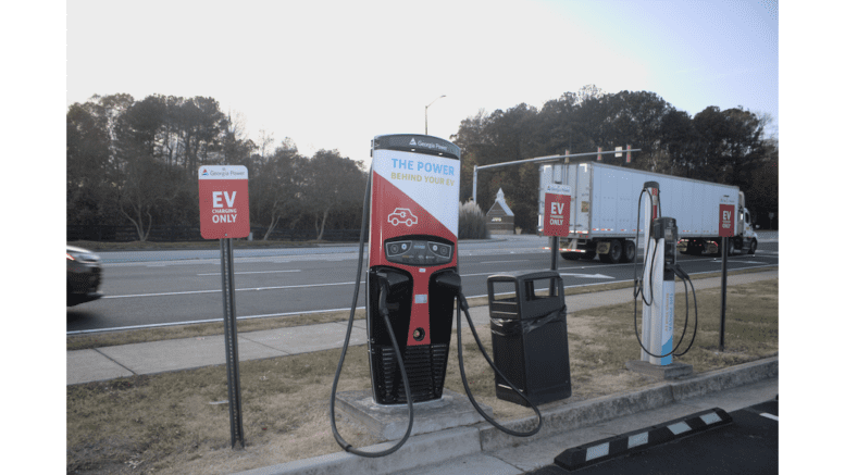 An electric vehicle charging station on Riverside Parkway, a moving tractor-trailer visible on the roadway.