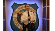 Cobb County Police Chief Stuart VanHoozer in front of large Cobb police badge emblem speaking toward camera with TV station microphones in front