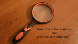 Magnifier on wooden table with the words Government transparency and freedom of information