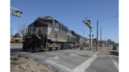 An Norfolk Southern engine pulling a long line of boxcar, tankers and other cars starting through a crossing in downtown Austell GA