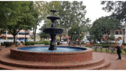 A brick fountain in Glover Park on Marietta Square. benches surround a circular brick path and a photographer snaps a shot.