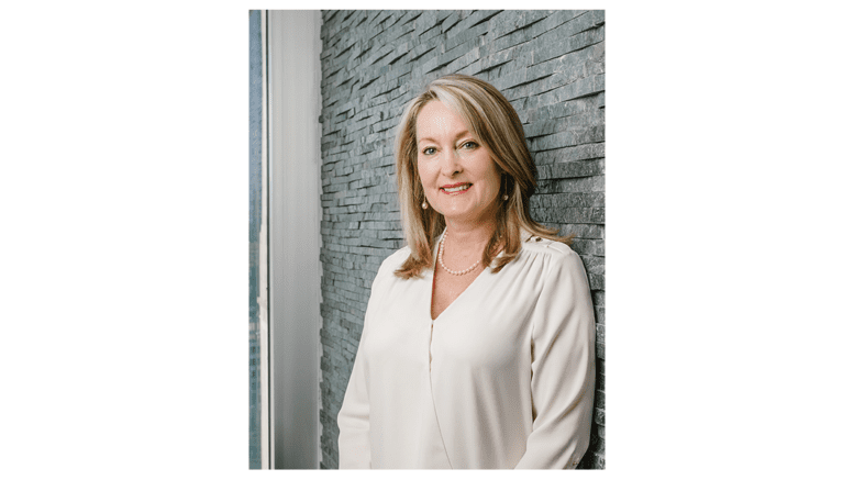 Jo Ann Chitty wearing a white shirt standing against a wall.