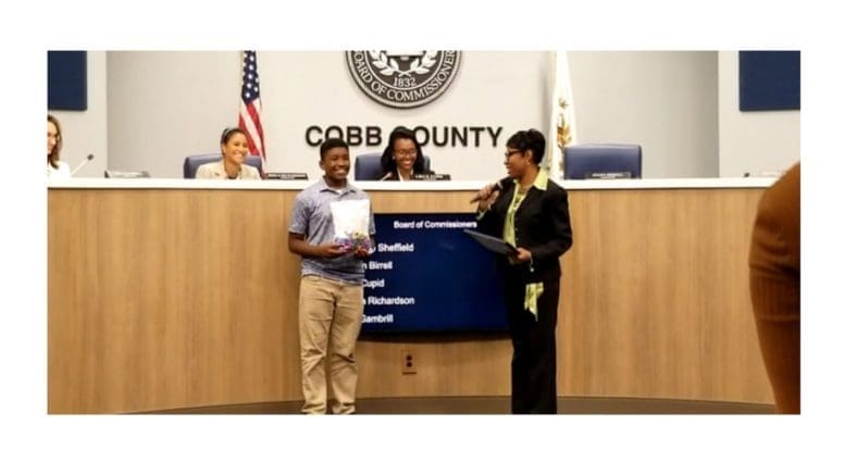 A young man holding a certificate with Commissioner Monique Sheffield