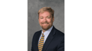 Upper body shot of Chris Britton, smiling, beard and moustache, dark coat and striped tie