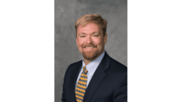 Upper body shot of Chris Britton, smiling, beard and moustache, dark coat and striped tie