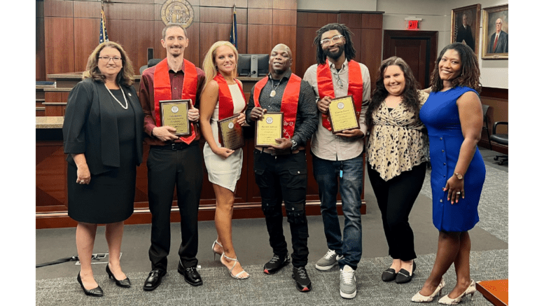 A row of officials and drug treatment court graduates, some holding certificates