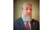 Klay Kilcrease bearded with a blue suit and striped tie.