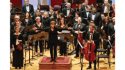 Tamara Dworetz stands armed outstretched on a podium in front of a small orchestra