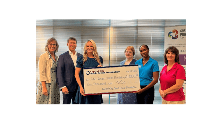 A group of five women and one man, two of the women holding up a large replica check