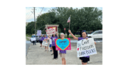 People waving signs protesting the banning of books by the Cobb County School District