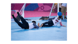 Two visually-impaired goalball athletes diving for the ball in front of a net