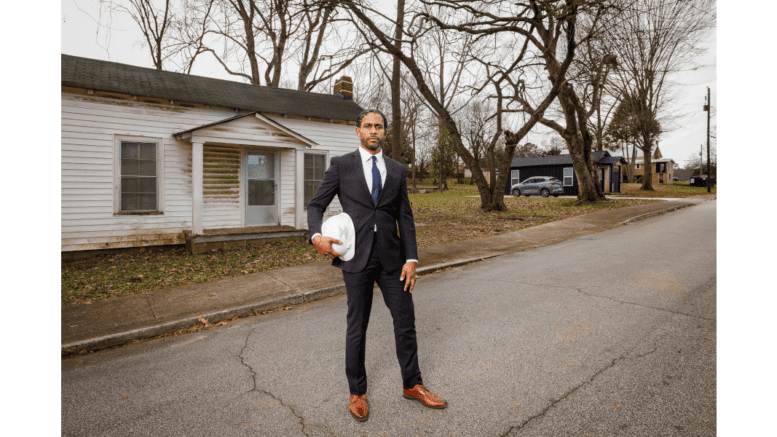 Derek Caffe holding a hard hat stands in front of an aging house