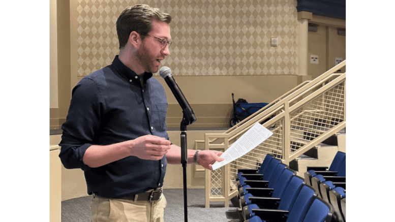 Andrew Cole speaking at a standup microphone